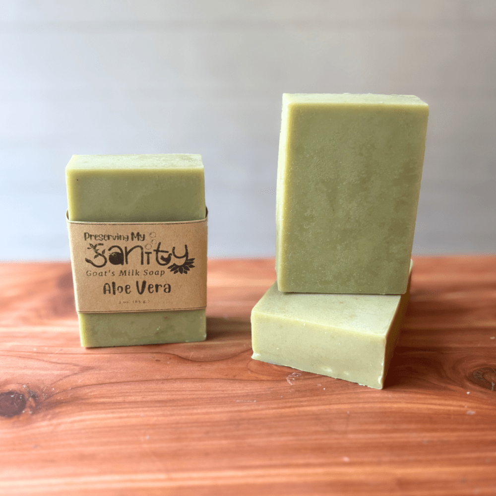 Photo of three bars of aloe vera and essential oil goat milk soap displayed to show design, top, and label