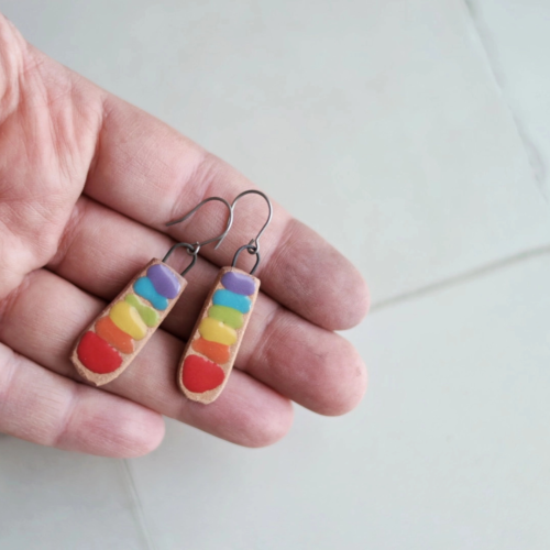 Photo of someone's hand holding a pair of rainbow chakra bar ceramic earrings