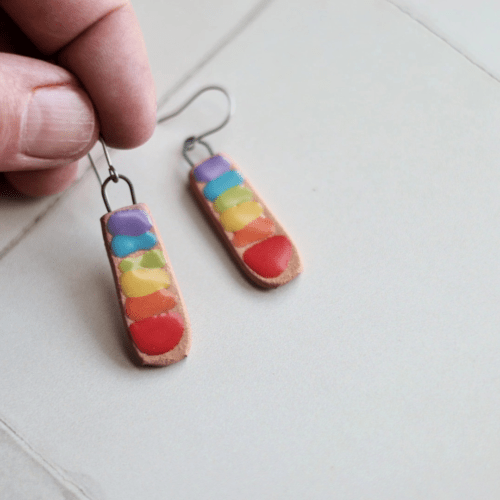 Photo of someone's finger holding a pair of rainbow chakra bar ceramic earrings