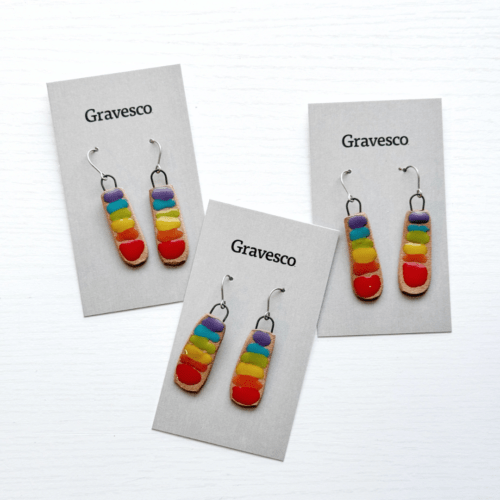 Flatlay photo showing three pairs of rainbow chakra bar ceramic earrings, with white wood background