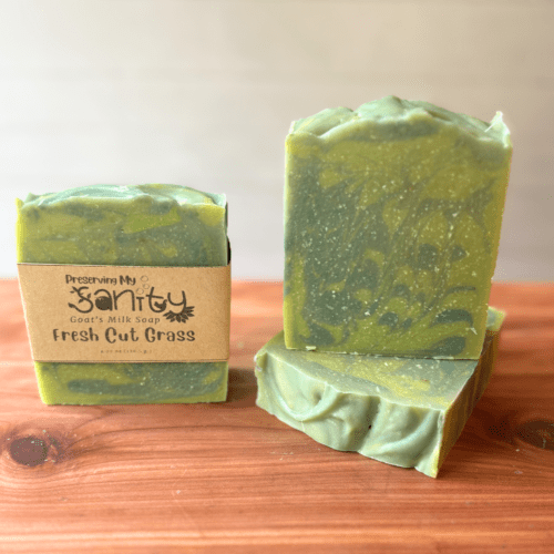 Photo of three bars of fresh cut grass goat milk soap displayed to show design, top, and label