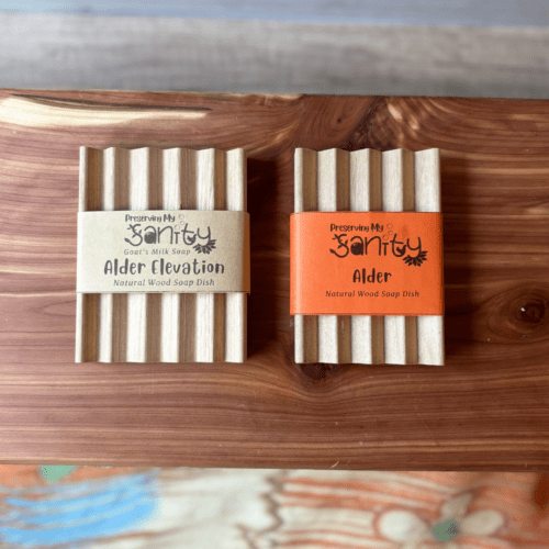 Flatlay photo showing a regular alder natural wood soap dish beside an elevation-style alder natural wood soap dish - both made in the USA