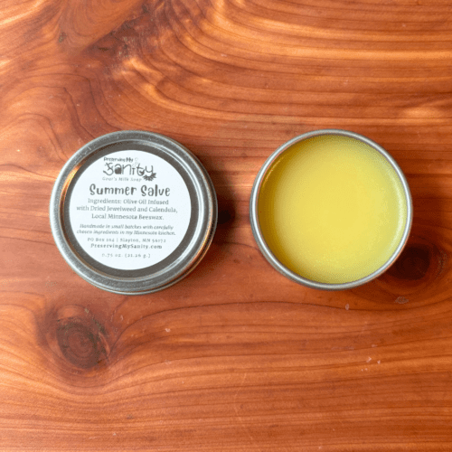 Flatlay photo of a 1-ounce tin of summer salve, which is made with calendula and jewelweed infused olive oil and local Minnesota beeswax. Sold in an aluminum tin with screwtop.