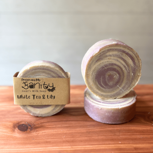 Photo of three round bars of white tea and lily goat milk soap displayed to show design, top, and label