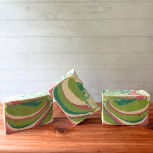 Closeup photo showing three bars of Lush Succulent goat milk soap on a finished cedar board with a whitewashed wood background