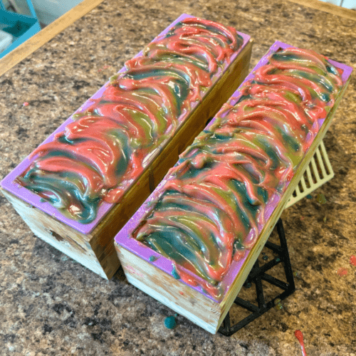 Process photo showing two freshly poured loaves of apple sage goat milk soap with textured tops.