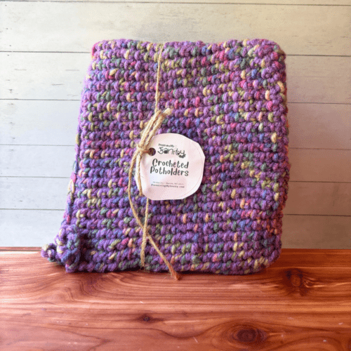 Set of two crocheted potholders with purple as the main color stitched with a multi color variegated yarn.