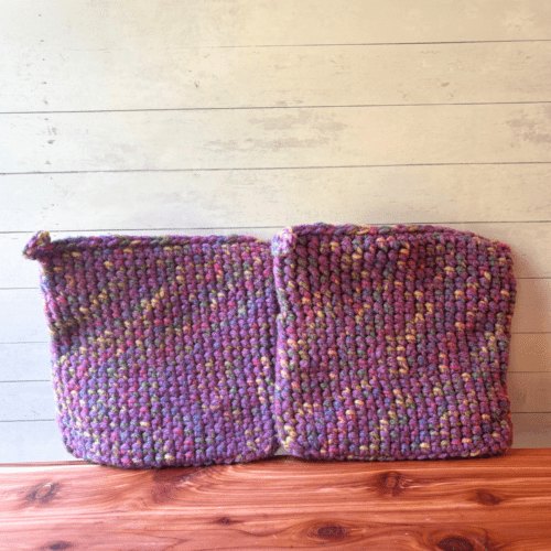 Set of two crocheted potholders with purple as the main color stitched with a multi color variegated yarn.