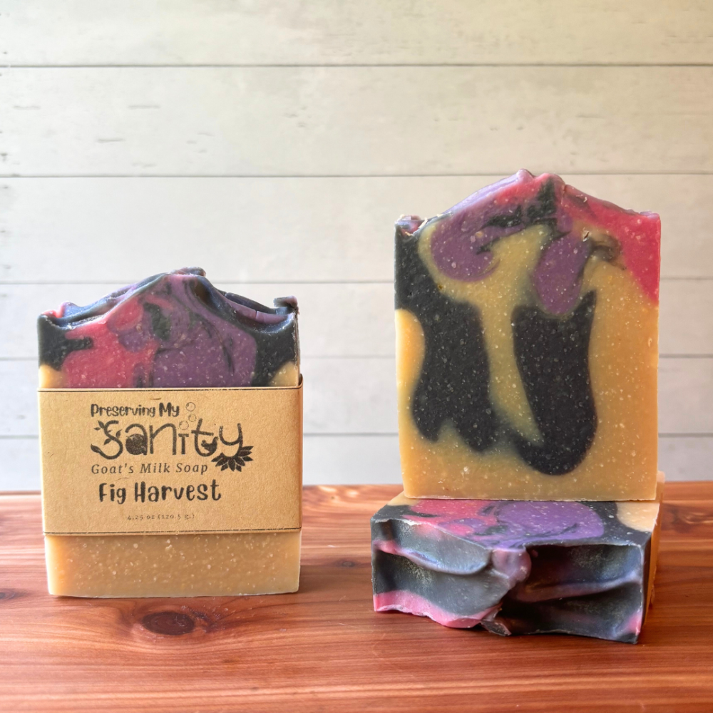 Display photo showcasing three bars of Fig Harvest goat milk soap, part of the fall collection. Colors were drop swirled into plain batter and include dark gray, medium purple, and bright pink.