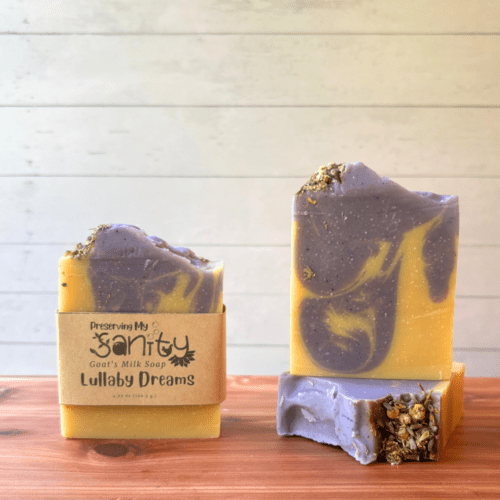 Display photo showcasing three bars of Lullaby Dreams goat milk soap featuring a lovely fragrance blend of lavender and chamomile. The bars are yellow and lavender and have dried chamomile flowers on top.