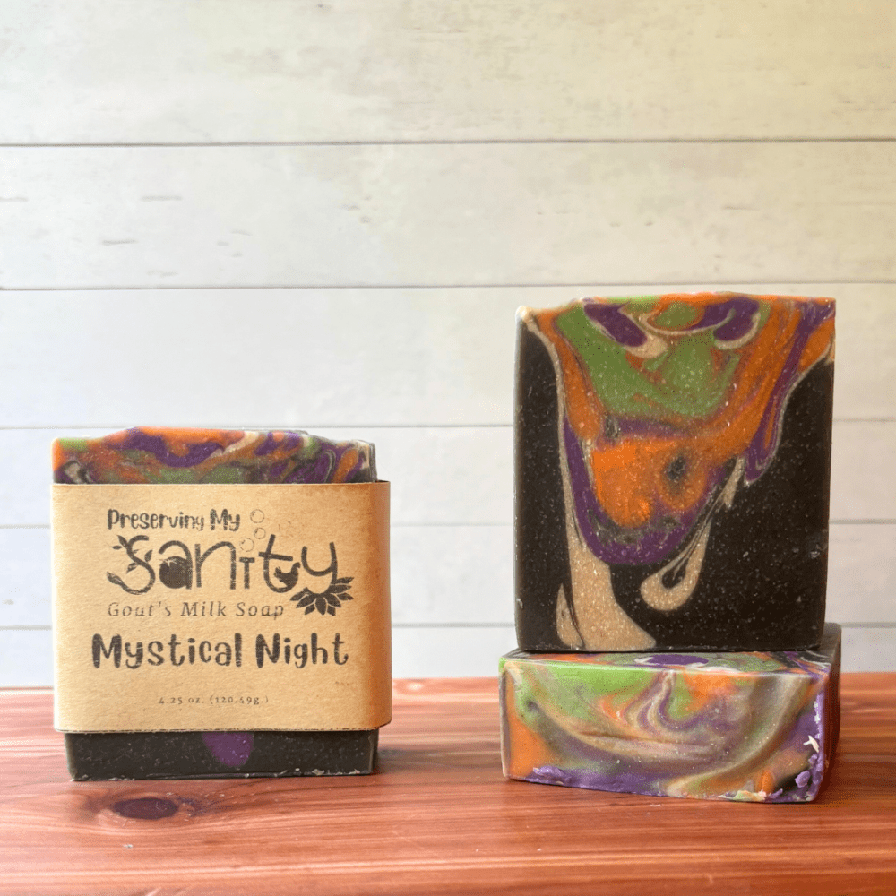 Display photo showcasing three bars of Mystical Night Halloween goat milk soap, handcrafted in small batches in Minnesota. These drop swirl bars feature black, white, purple, orange, and green and are scented with a dark and dreamy fragrance that's perfect for this fun holiday.