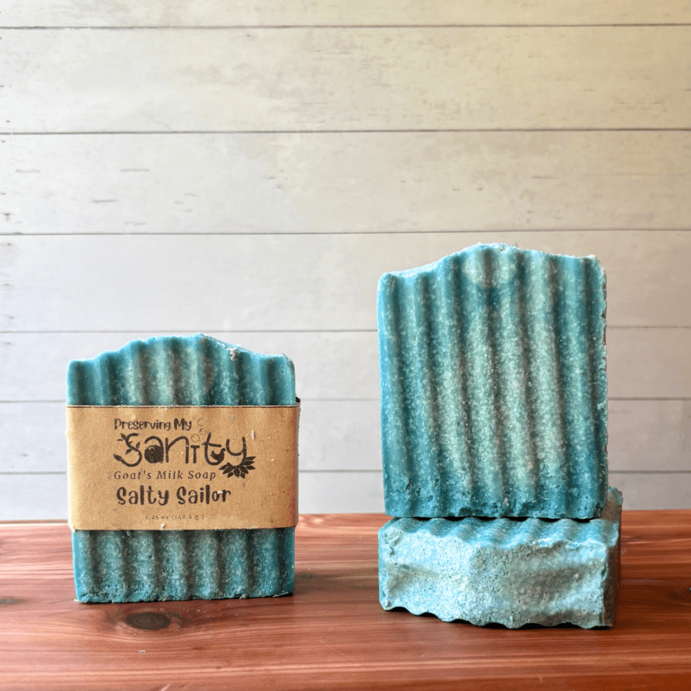 Front view of three bars of Salty Sailor sea salt soap. One bar shows a soap label, the other two are displayed to show different angles of the soap. The bars are an aqua blue color with a hint of white swirls. This handcrafted goat milk soap is handcrafted in small batches in Minnesota with local goat milk.