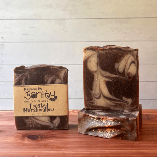 Display photo showcasing three bars of handcrafted Toasted Marshallow goat milk soap, one bar with a label and the other two without labels to show the pretty dark brown swirls in this artisan soap. The bars are lightly topped with some copper mica.