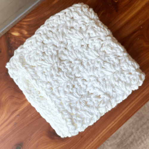 Overhead flat lay photo of a pretty white crocheted washcloth folded in quarters on top of a cedar bath board.