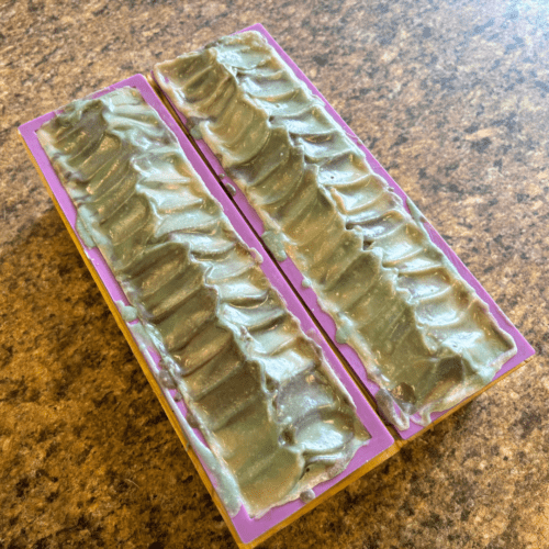 Process photo showing two loaves of freshly poured Wild Woods goat milk soap in molds with textured tops.