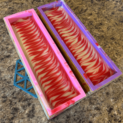 Process photo showing two full loaves of freshly poured Candy Cane goat milk soap with a Taiwan Swirl pattern on top