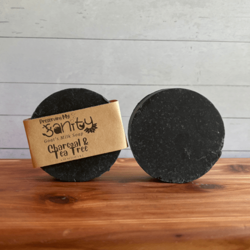 Photo of two round bars of charcoal and tea tree goat milk soap arranged to show different angles and parts of handcrafted soap bars