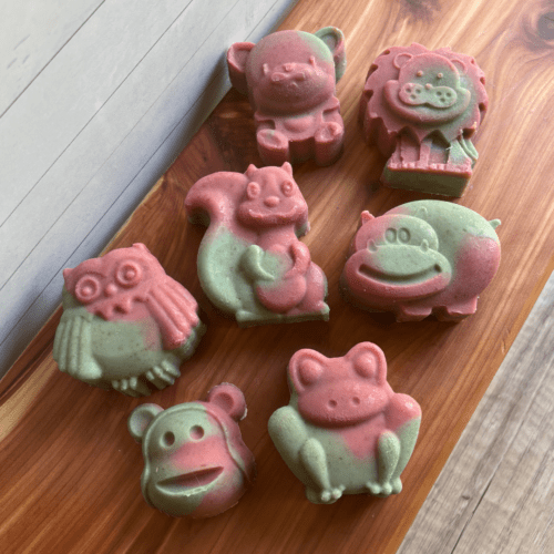 Collage photo showcasing a variety of animal shaped goat milk soap in cotton candy scent and a blue and pink design. Animals pictured include lion, bear, squirrel, hippo, owl, frog, and monkey.