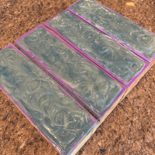 Process photo showing four loaves of freshly poured Fresh Snow goat milk soap with biodegradable glitter and swirls on top.