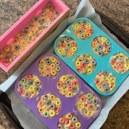 Process photo showing two types of fruit cereal circles goat milk soap in molds - round bars and what will become square bars. Decorated with colorful loops made with colored soap batter.