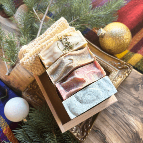 Alternate overhead flatlay view of four bars of full size holiday soap pictured with a soap saver bag and reclaimed wood gift tray, included in the holiday soap bundle