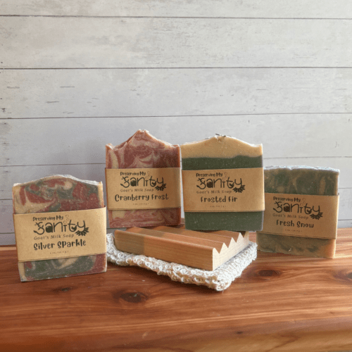 Photo of four half size bars of goat milk soap with a natural wood soap dish and sisal soap saver bag, all included in the holiday soap sampler.