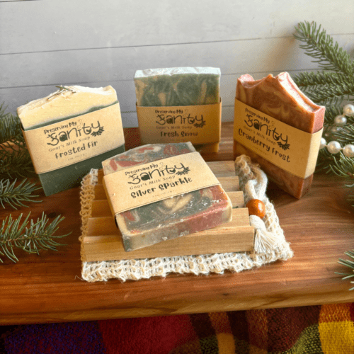 Alternate view display photo showing four half-size bars of holiday goat milk soap with a soap dish and soap bag