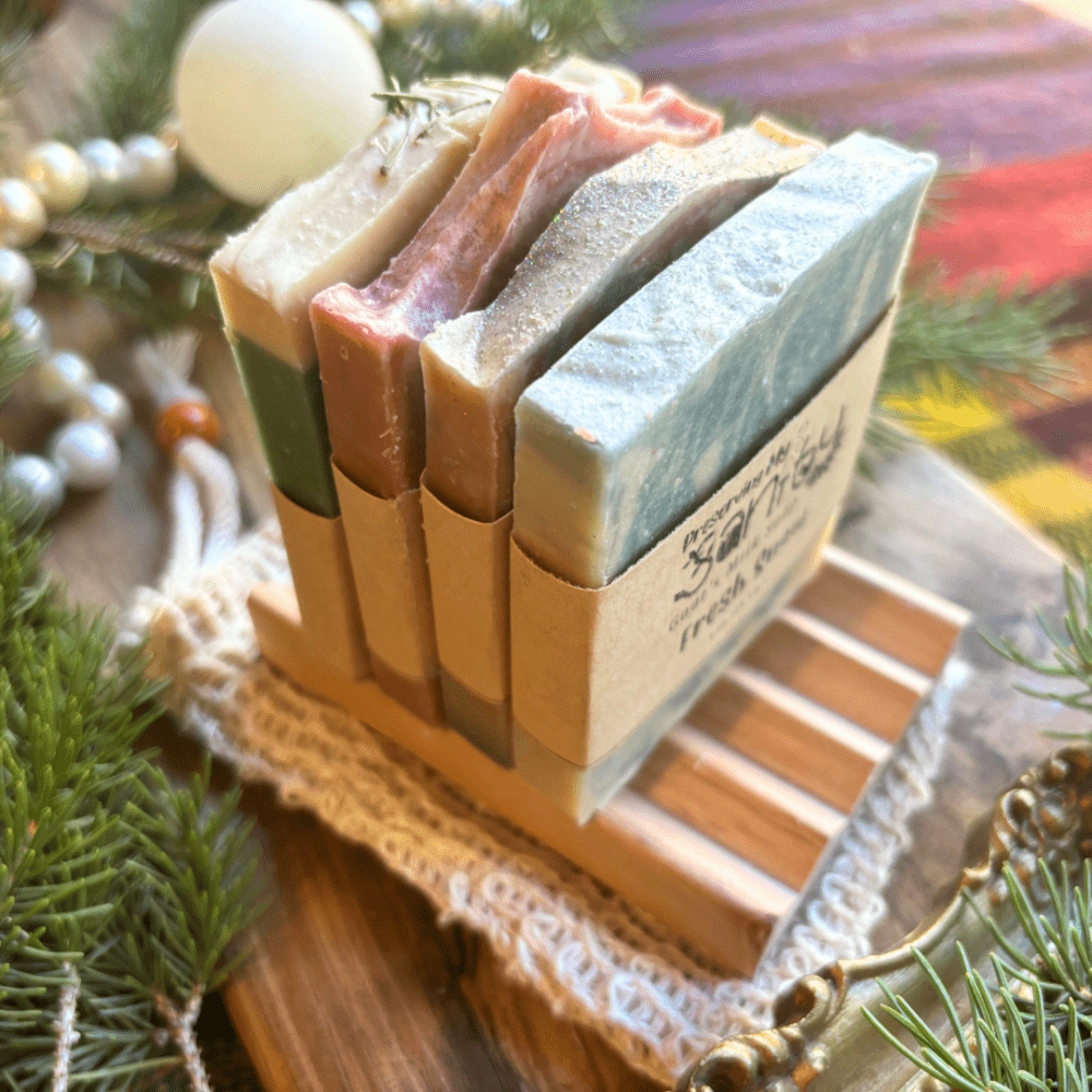 Top and side view showcasing four half-size bars of holiday goat milk soap with a soap dish and soap saver bag