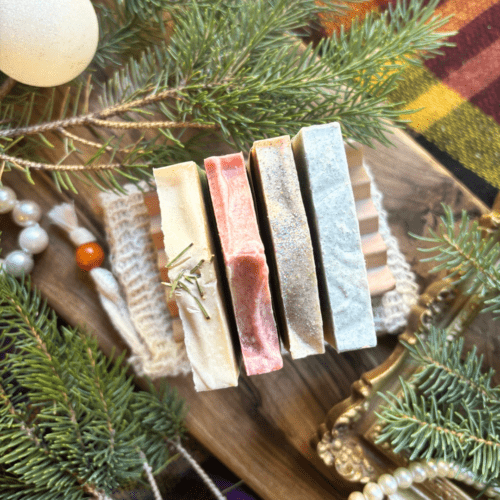 Overhead view of four half-size bars of soap, sitting on a natural wood soap dish and soap saver bag