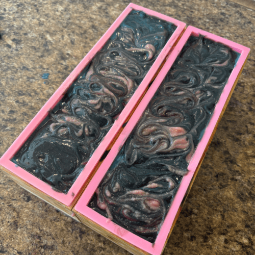 Process photo showing two freshly poured loaves of Party Dress goat milk soap with swirled tops.