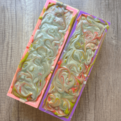 Process photo showing two loaves of freshly poured Santa's Elves goat milk soap with colorful swirled design on top