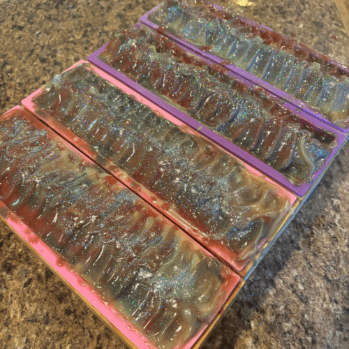 Process photo showing four freshly poured loaves of Silver Sparkle goat milk soap with biodegradable glitter and textured tops