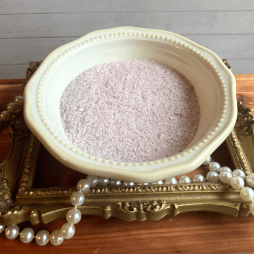 Small bowl of Lavender Green Tea bath salt sitting on a gold frame with pearls