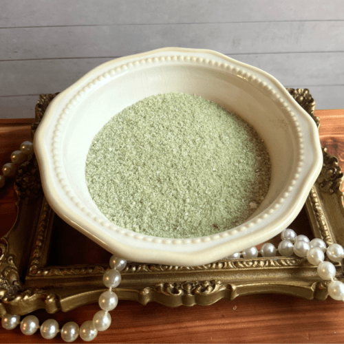 Small bowl of green Lemongrass Coconut bath salt sitting on a gold frame with pearls