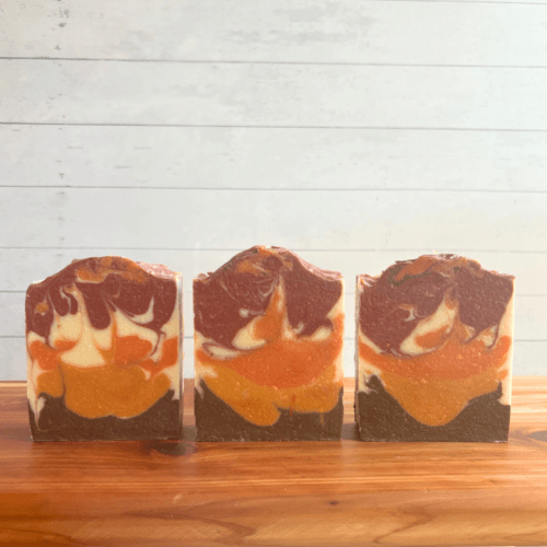 Alternate view of three bars of Cowboy goat milk soap, none with labels to showcase the bonfire-type swirl pattern with 5 colors