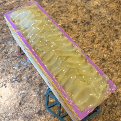 Process photo showcasing a freshly poured loaf of Lavender Patchouli goat milk soap with a pretty textured top