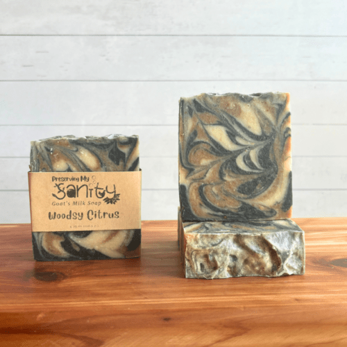 Front view display photo showcasing three pretty bars of Woodsy Citrus goat milk soap with essential oils and swirls of brown, black, and cream