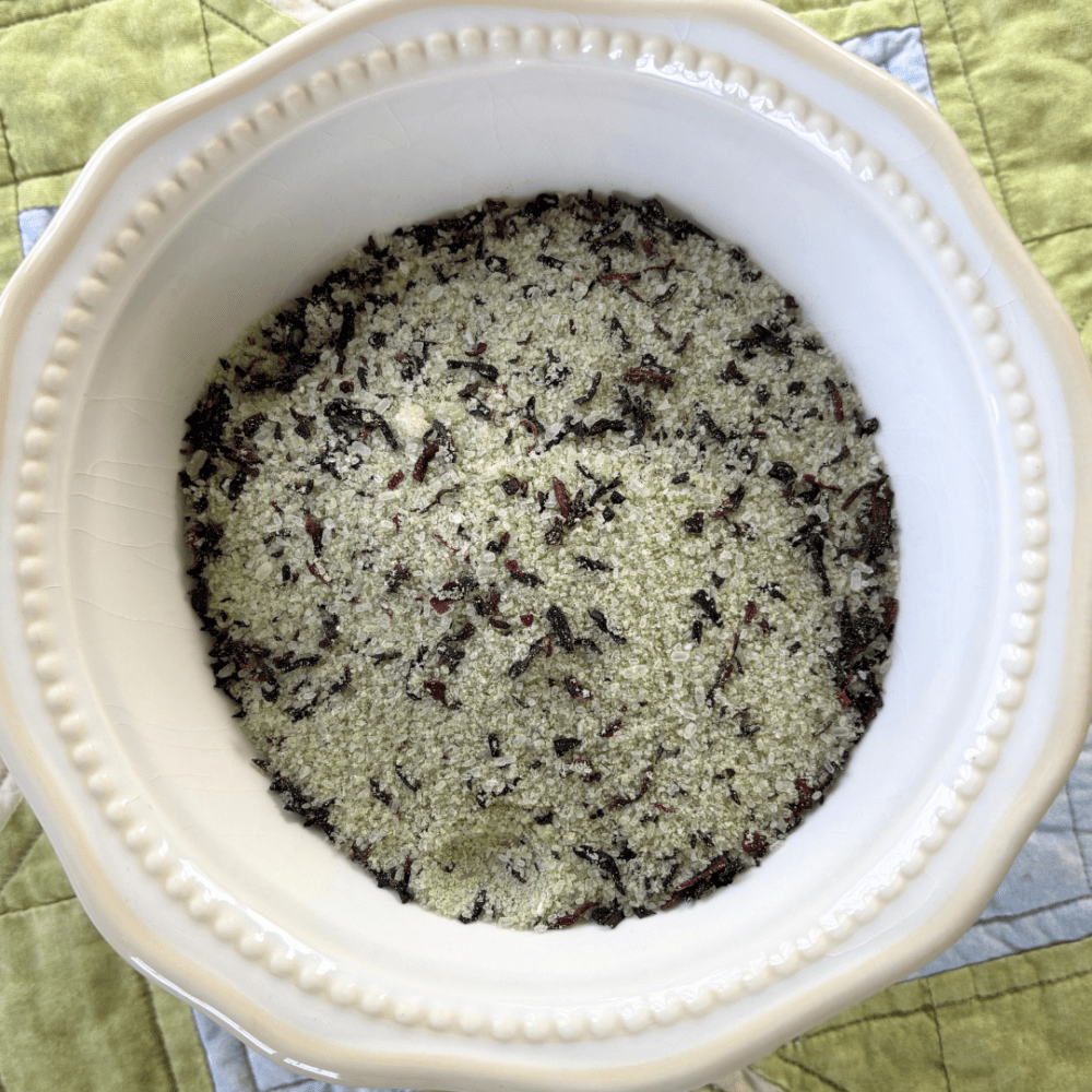 Pretty white bowl filled with lemongrass, coconut, and hibiscus bath tea, sitting on a spring tablecloth