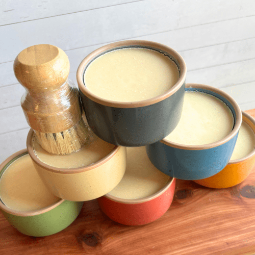 Display photo showcasing six colorful ramekins of cold process dish soap made with coconut oil and essential oils. Pictured with an eco-friendly bamboo dish brush.