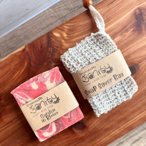 Half size bar of Garden in Bloom goat milk soap laying beside a sisal soap saver bag on a cedar bath board. This combination makes a great Valentine's Day gift for teachers and friends!