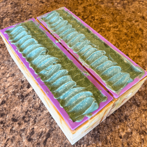 Process photo showing two full loaves of White Tea and Sage goat milk soap before it is cut into bars. The soap is green with a textured top that was created using a spoon.