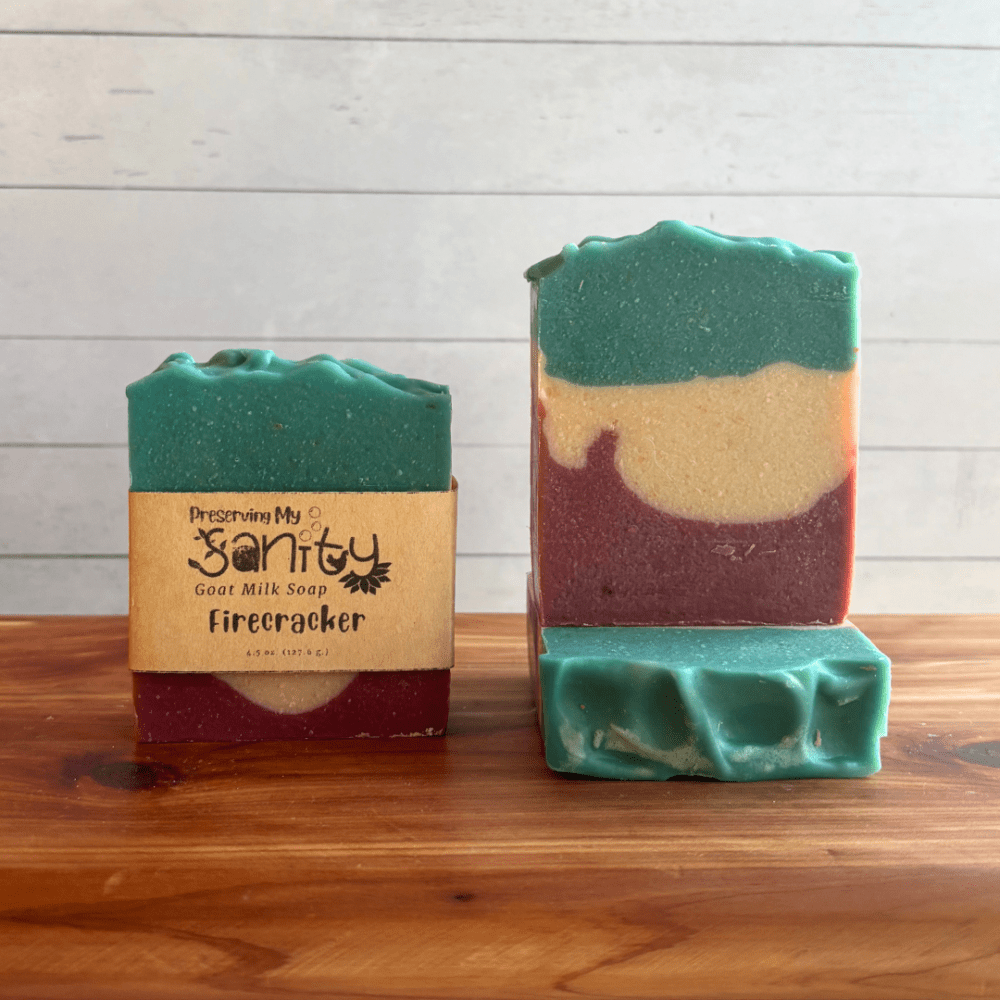 Alternate view display photo showcasing three bars of Firecracker goat milk soap sitting on a cedar board with a white shiplap background. This soap was inspired by everyone's favorite summer treat - the Firecracker Popsicle! The bottom layer is dark red, middle layer white, and top layer a pretty aqua blue. The fragrance is a mixed berry and vanilla one, which goes perfectly with this design!