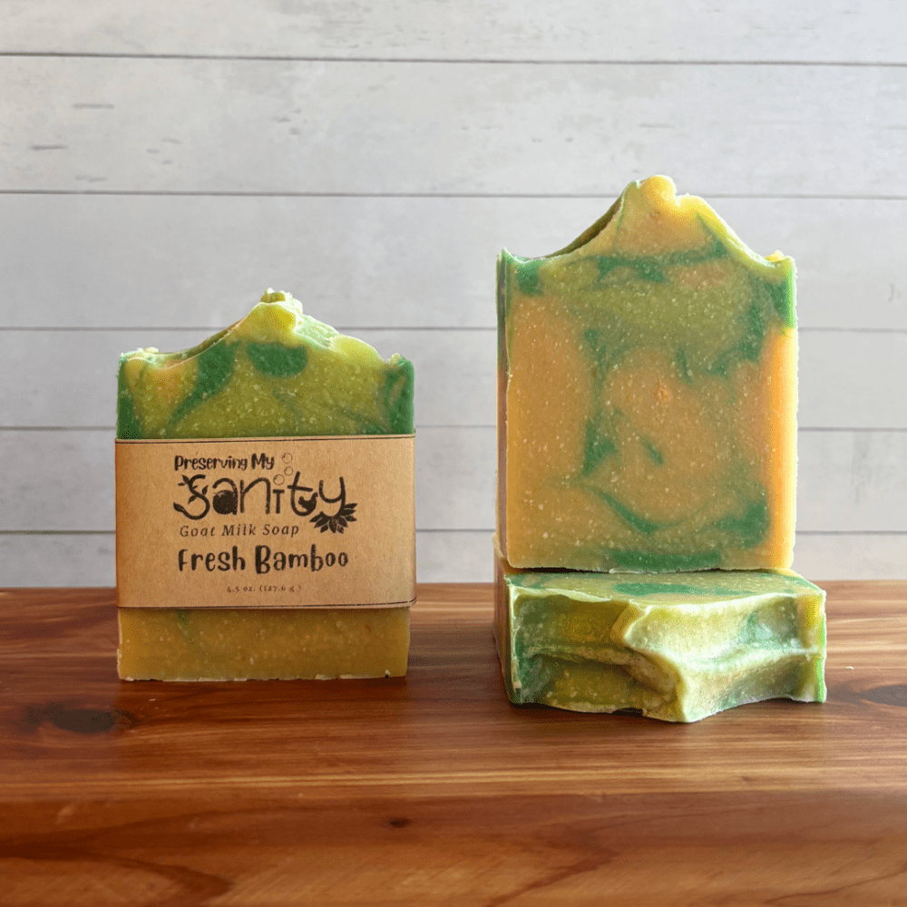 Alternate view display photo showcasing three bars of Fresh Bamboo goat milk soap sitting on a cedar board with a white shiplap background. This colorful soap has a bright yellow base and subtle bright green swirls into it, and the scent is a fresh and clean one that's great for spring!