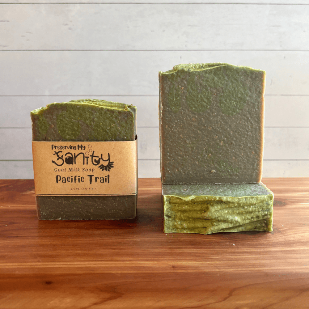 Alternate view of display photo showcasing three bars of Pacific Trail soap sitting on a cedar board with a white shiplap background. The soap is a dark gray color with some dark green swirled into it, which is kind of hard to see in the photo.