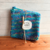Set of two blue variegated crocheted potholders on a cedar bath board, tied with a piece of twine with a simple brand label.