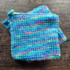 Set of two variegated blue crocheted potholders sitting on top of each other with a dark piece of wood as the backdrop.
