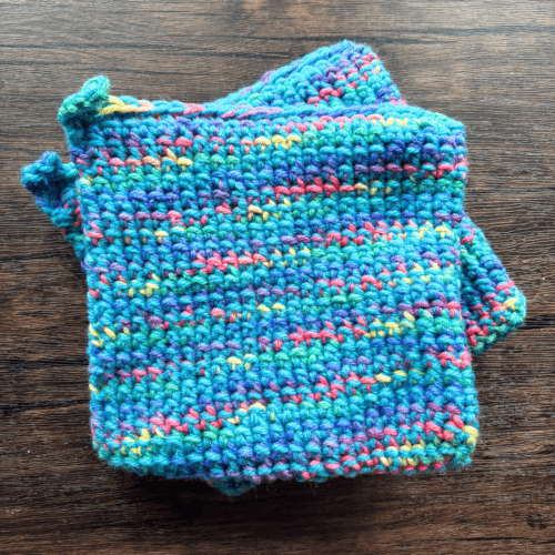 Set of two variegated blue crocheted potholders sitting on top of each other with a dark piece of wood as the backdrop.