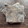 Set of two variegated gray and beige crocheted potholders sitting on top of each other with a dark piece of wood as the backdrop.