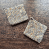 Set of two variegated gray and beige crocheted potholders arranged separately on a dark piece of wood as the backdrop.