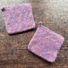 Set of two variegated purple crocheted potholders arranged separately on a dark piece of wood as the backdrop.